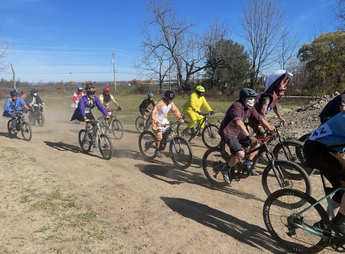 Cyclists in Halloween costumes racing on a dirt trail at Halloween Classic CX 2025 in Trumansburg, New York