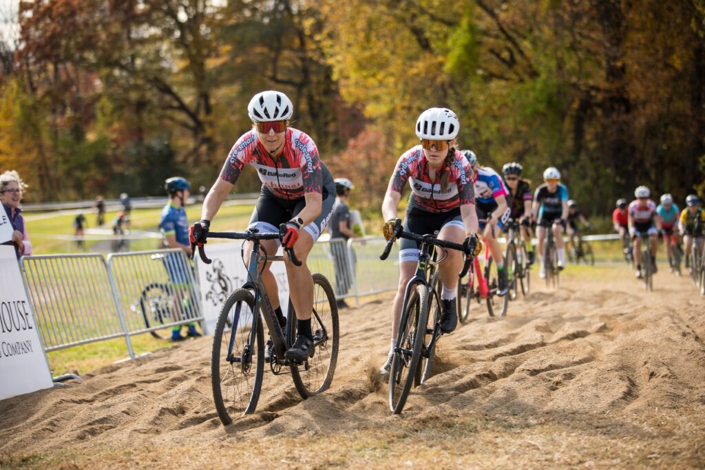 Annabelle and Alix Norris racing side by side through a sandy cyclocross section for the BikeReg | Share Coffee women’s cycling team.