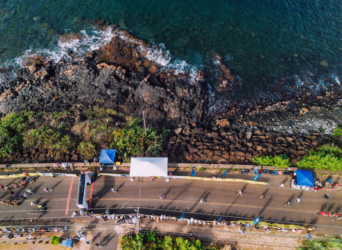 Aerial view of runners crossing the finish line along the ocean at the Kauai Marathon and Half Marathon in Hawaii.