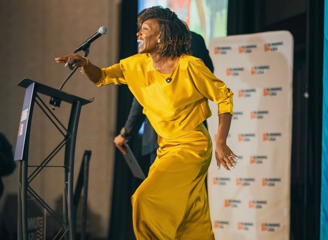 Dawn Harper-Nelson delivering a keynote presentation on stage at the Running USA Conference, speaking to event directors about inspiration and resilience.