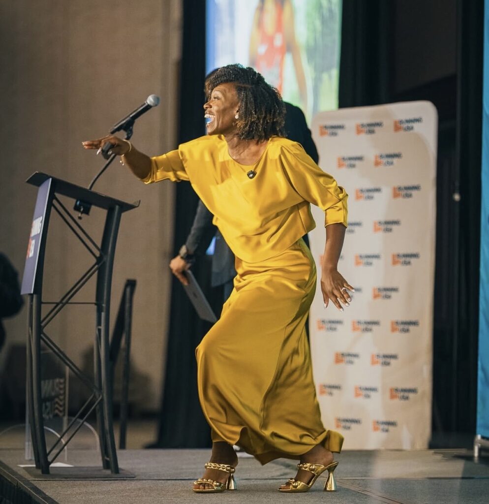 Dawn Harper-Nelson delivering a keynote presentation on stage at the Running USA Conference, speaking to event directors about inspiration and resilience.
