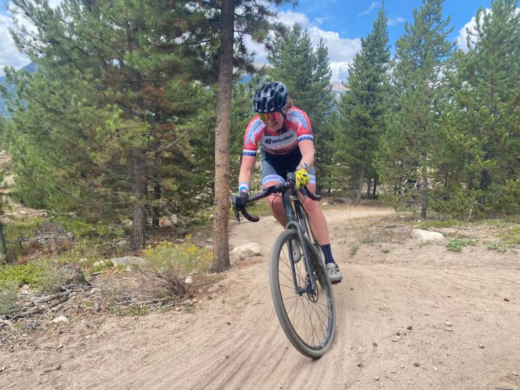 Annie Laurie Hines of the BikeReg | Share Coffee team racing a gravel bike on a wooded dirt course during the 2025 season.
