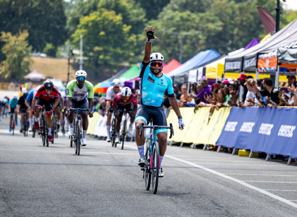 Cyclist celebrating a solo finish at Chocolate City Criterium with crowd cheering along a colorful, festival-style race course.
