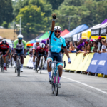 Cyclist celebrating a solo finish at Chocolate City Criterium with crowd cheering along a colorful, festival-style race course.