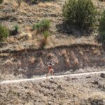 A trail runner races along a dirt road cut into a high-desert hillside dotted with yucca and juniper at the Daydreamer trail run in Patagonia, Arizona.