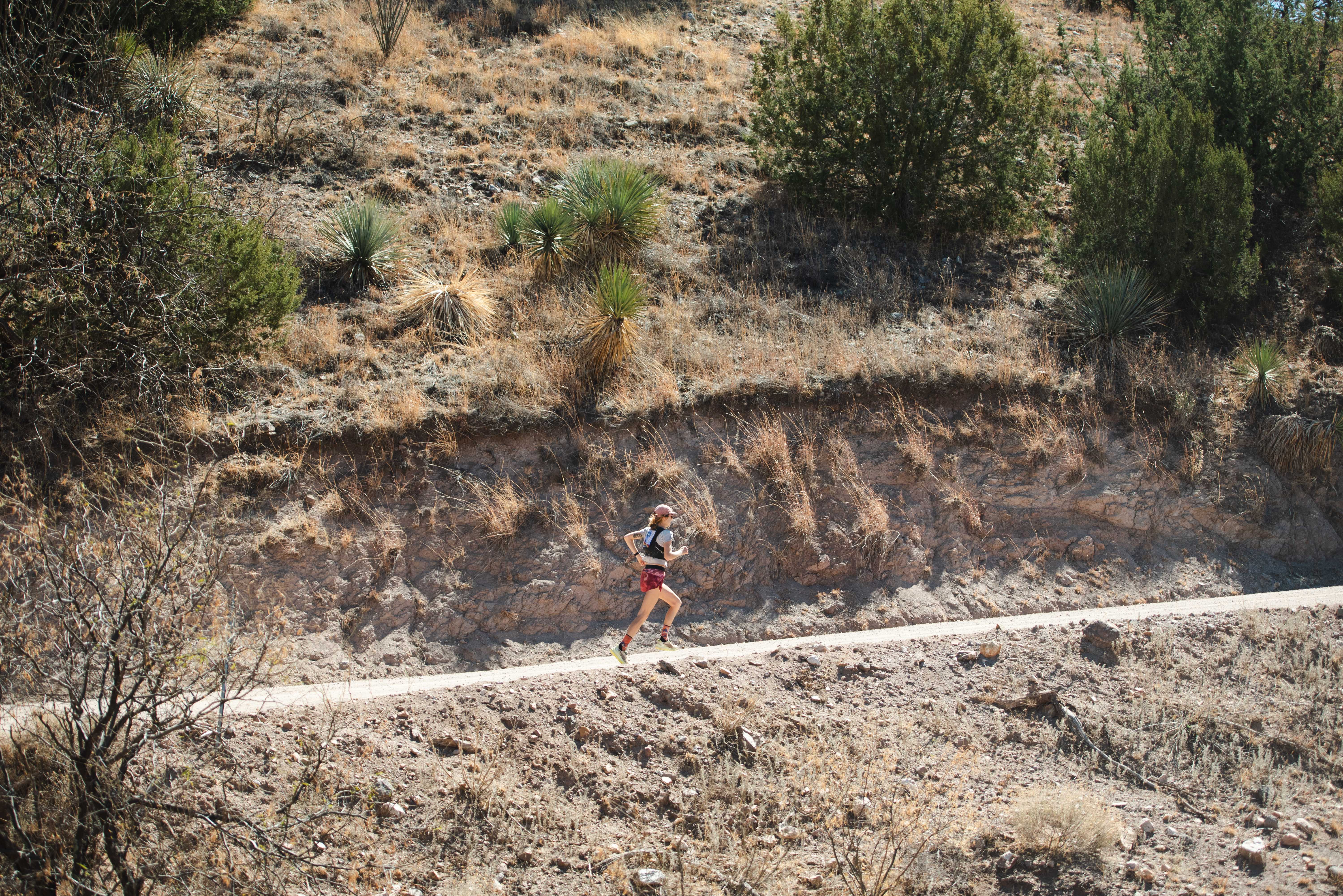 A trail runner races along a dirt road cut into a high-desert hillside dotted with yucca and juniper at the Daydreamer trail run in Patagonia, Arizona.